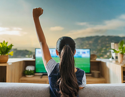an ai-generated image of a brown-haired teenage girl in a blue-and-white outfit watching TV and putting her fist in the air triumphantly