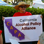 Woman in large hat proudly holds up CAPA California Alcohol Policy Alliance banner